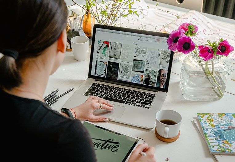 A person using laptop for graphic designs on a table with a cup of coffee