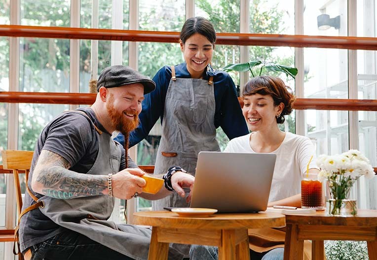 Three happy colleagues working on a laptop in cafe