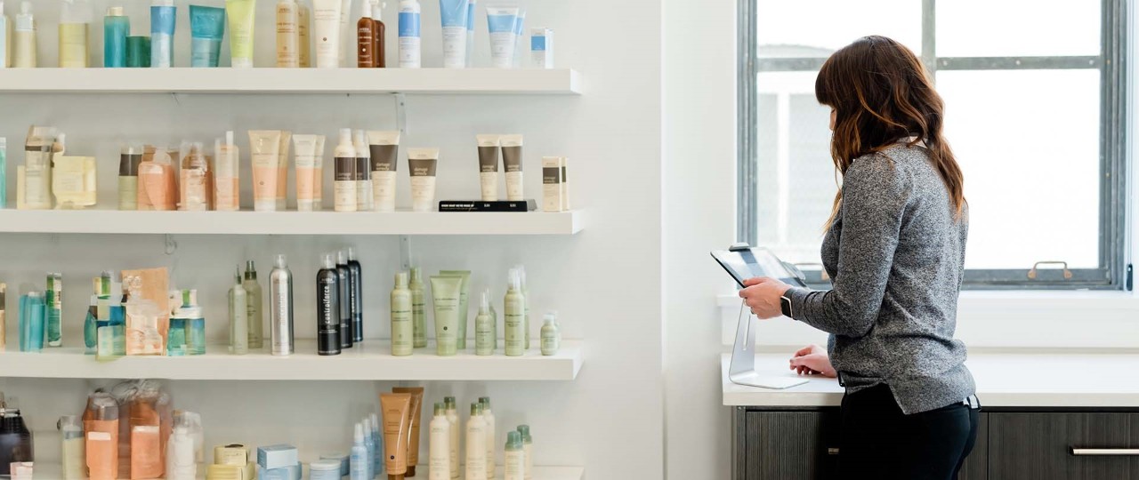 A woman in a grey sweater holding a tablet in a hair salon