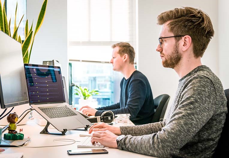 Two people sitting on chairs working on their laptops in an office environment