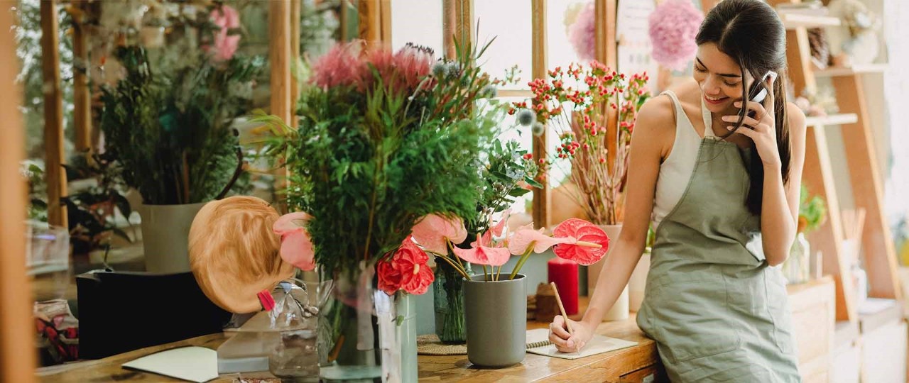 Happy woman talking on a smartphone while working in a florist shop