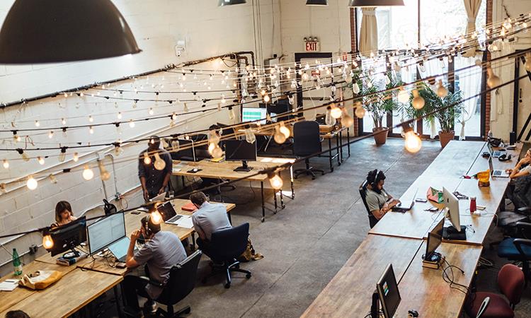 Group of people using laptops sat on a table together in an office environment