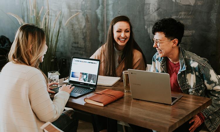 Three people sitting in front of a table laughing together