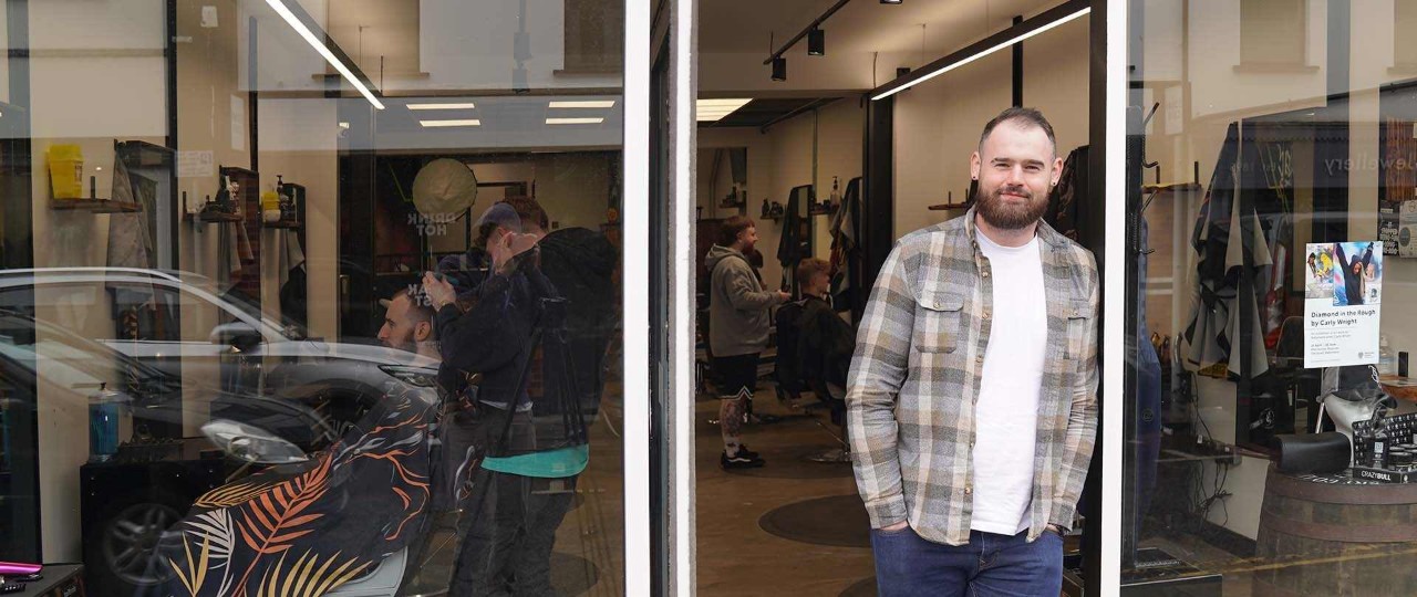 The owner of the Barber Collective, Barry Johnson, standing outside his shop smiling