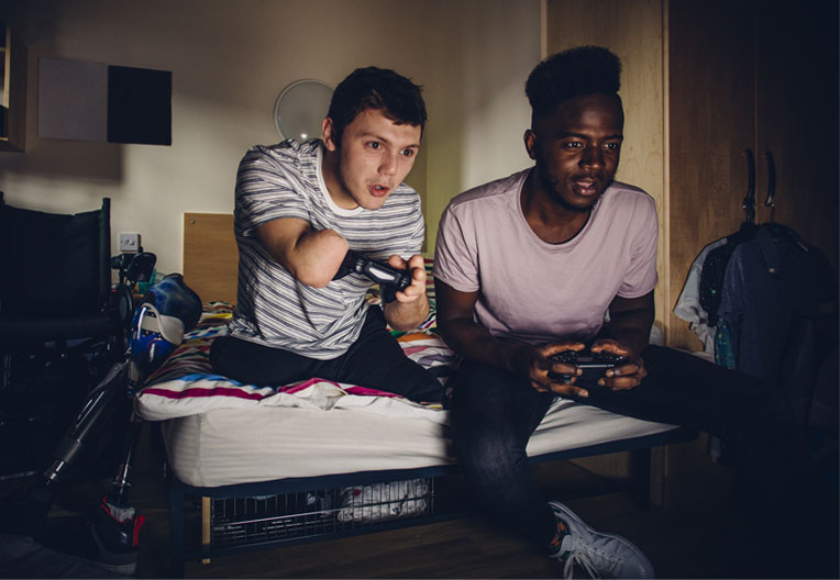 Two students playing on a game console with his friend, in student accommodation