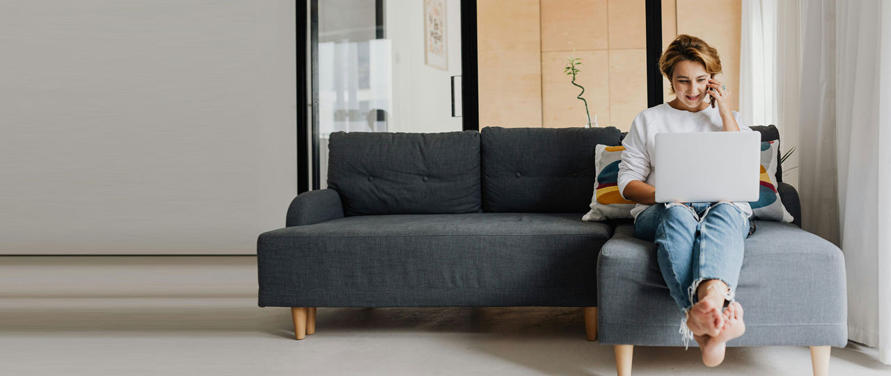 Woman talking on the phone with a laptop whilst sitting on the sofa.