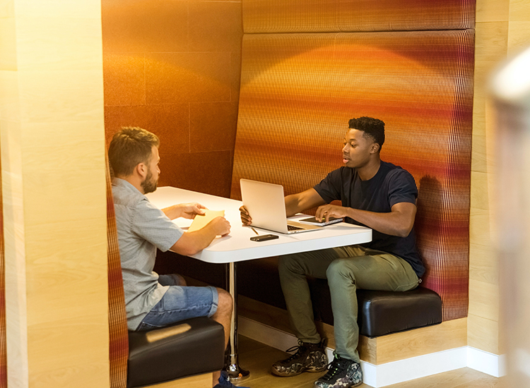 Two men sitting on a black leather bench with the laptops