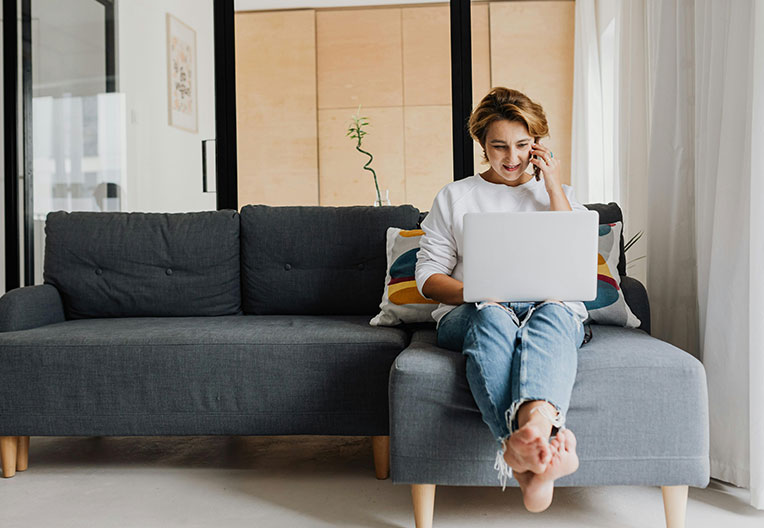 Woman talking on the phone with a laptop whilst sitting on the sofa.