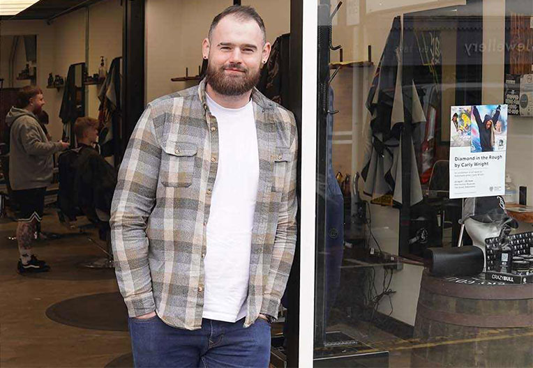 The owner of the Barber Collective, Barry Johnson, standing outside his shop smiling