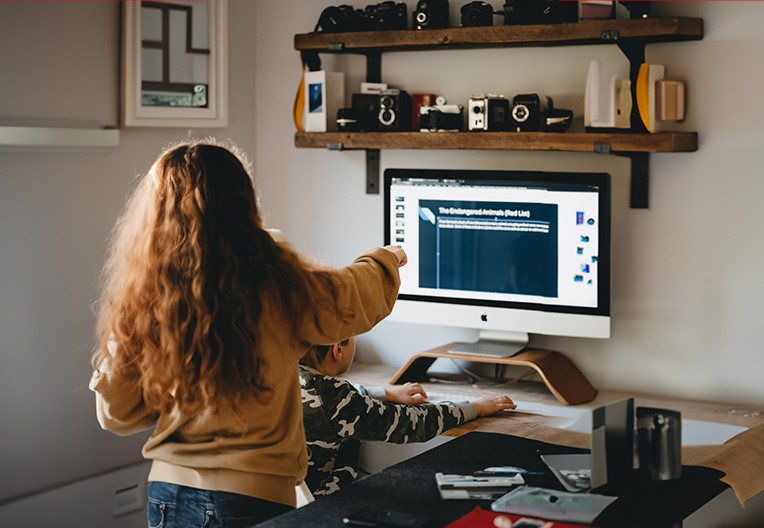 A woman and young boy t sitting in front of a silver iMac