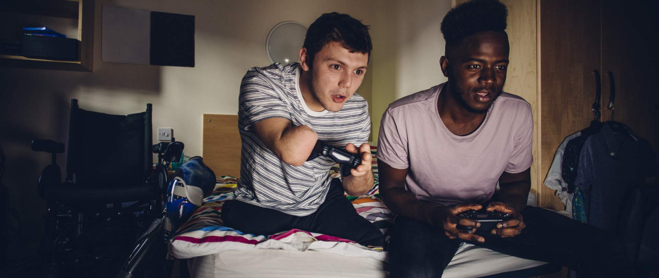Two students playing on a game console with his friend, in student accommodation