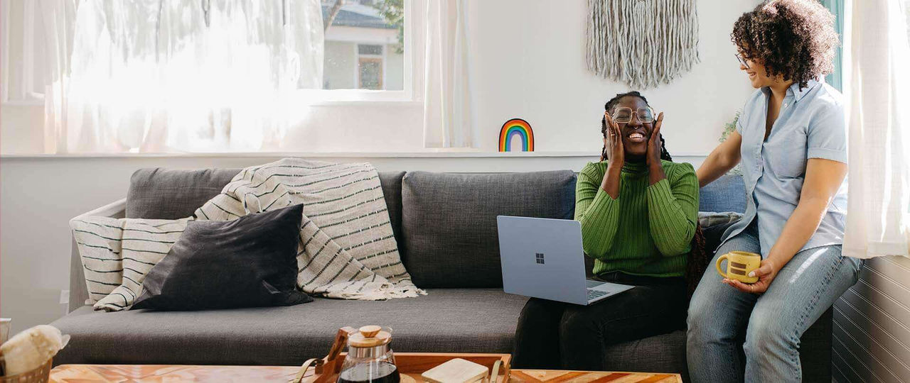 Two women sitting on a couch talking with a laptop