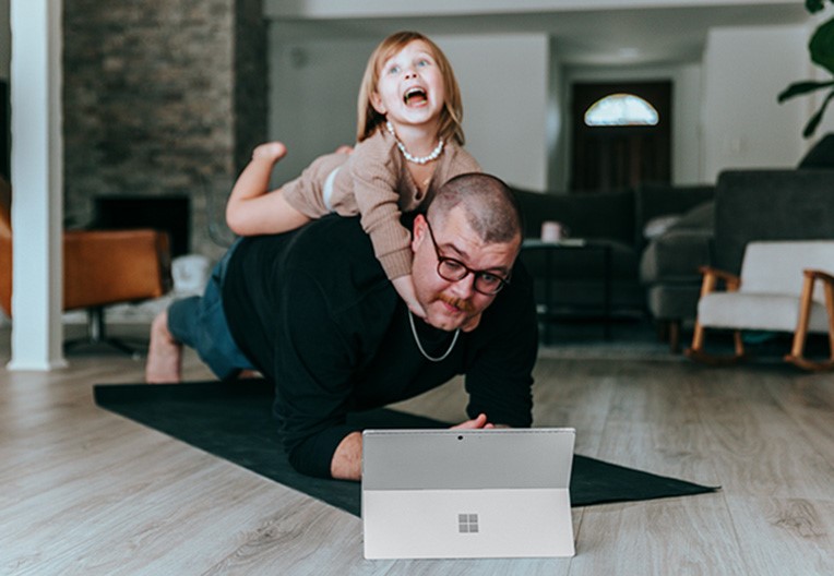 A man and a little girl playing with a laptop with the girl on his back