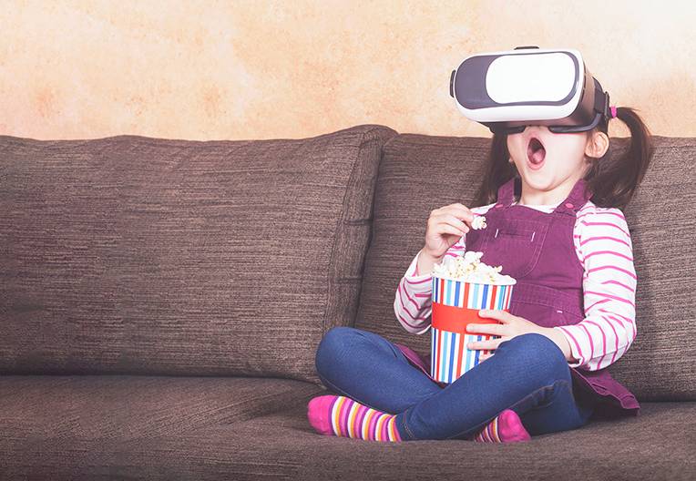 Excited little girl experiencing virtual reality at home whilst eating popcorn