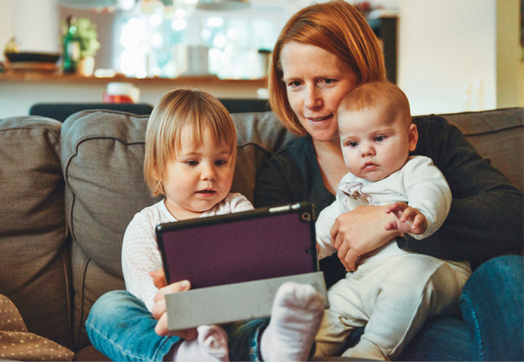 Mum and her two kids sat on a sofa with their tablet