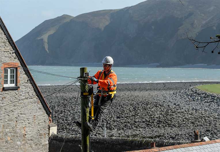 Openreach engineer climbing up a pole in a rural location