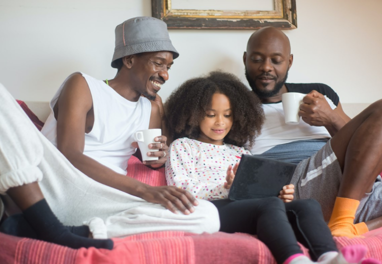 two adults and a child  smiling and playing on a tablet